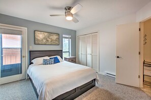 Ein Schlafzimmer mit einem Bett, einem Deckenventilator, einem Fenster mit Jalousien, einer Tür und einem an der Wand hängenden Kunstwerk.
