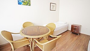 A room with a round glass table surrounded by wicker chairs, a bed with white bedding, a small wooden nightstand, and two framed pictures on the wall. - Bozcaada Balci Hotel (Bozcaada)