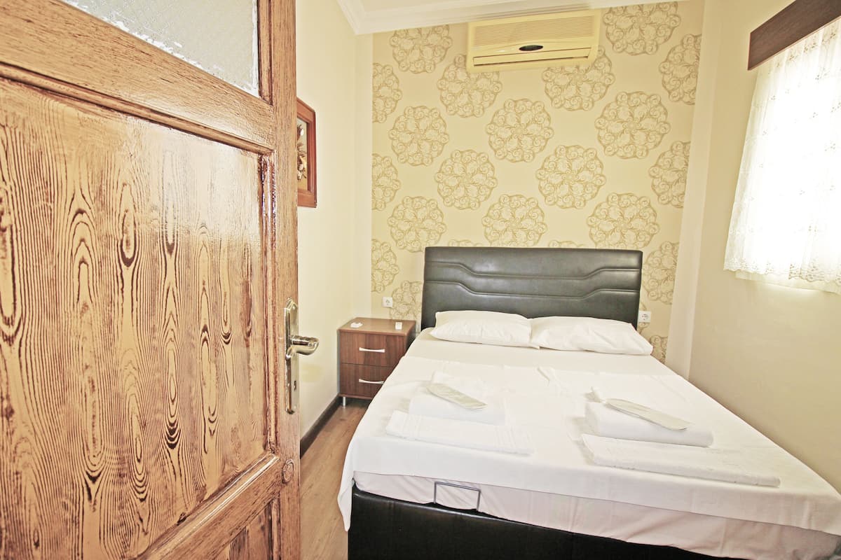 A neatly made bed with white linens and pillows, a wooden wardrobe, and a small bedside table with a lamp.