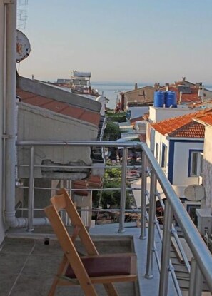 A balcony with a chair, a metal railing, and a view of the sea and buildings. - Bozcaada Balci Hotel (Bozcaada)