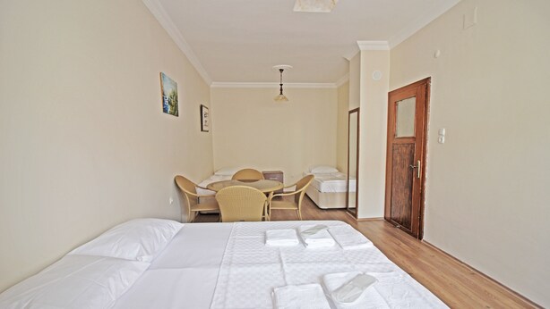A hotel room with a large bed, a desk with a chair, a small table, and a wooden door. - Bozcaada Balci Hotel (Bozcaada)