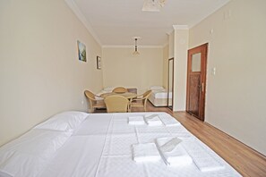 A hotel room with a large bed, a desk with a chair, a small table, and a wooden door. - Bozcaada Balci Hotel (Bozcaada)