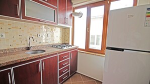 A kitchen with wooden cabinets, a sink, a stove, and a refrigerator. - Bozcaada Balci Hotel (Bozcaada)
