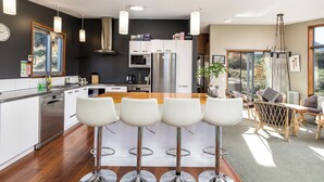 Una cocina moderna con una isla central, taburetes de bar y una zona de comedor con sillas de mimbre.