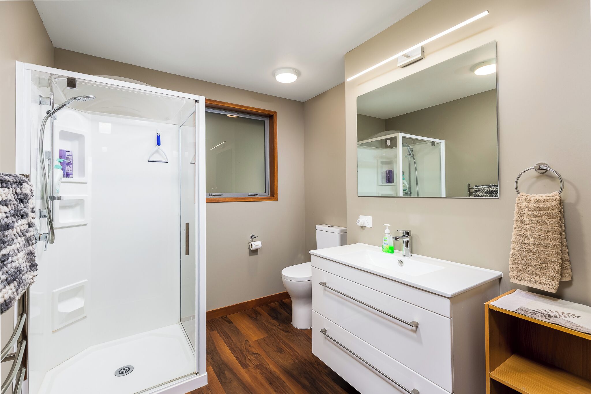 Un bany modern amb una dutxa envidrada per vidre, un lavabo blanc i un mirall gran.