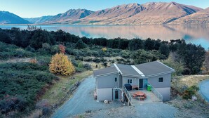 Una casa moderna con un patio, una pequeña terraza y vistas a un lago y montañas.