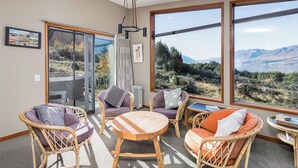 Un interior moderno con mobiliario de mimbre, ventanas amplias y vistas a montañas.