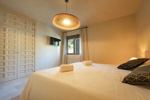 A bedroom with a bed, a television, a window with curtains, and a wall-mounted light fixture.