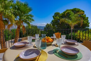 An outdoor dining area with a table set for two, surrounded by palm trees and a scenic view.