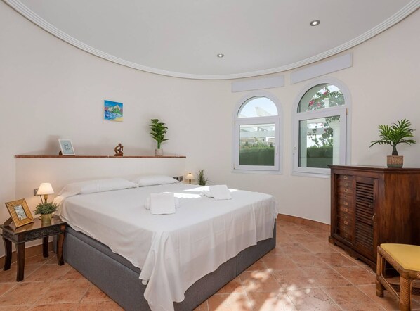 A bedroom with a bed, bedside tables, a dresser, and two windows.