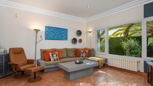 Una sala de estar con sofá, sillón y mesa de centro, un cuadro en la pared y un ventanal con vistas a zonas verdes.