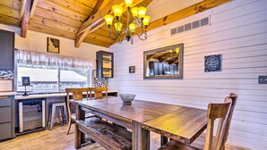 A wooden dining table with benches, a chandelier, and a kitchen area with a refrigerator and sink. - McCall Retreat w/ Hot Tub - 1/2 Mi to Downtown! (McCall)