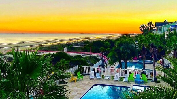 Un complexe hôtelier doté d’une piscine, de chaises longues et offrant une vue sur l’océan au coucher du soleil.