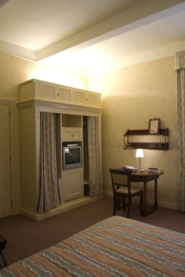 Habitación de hotel con cama, una pequeña mesa con silla, horno empotrado, estante con espejo y lámpara.