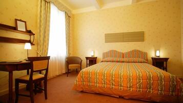 A hotel room with a bed, a desk, a chair, and a lamp.
