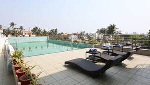 A rooftop pool area with lounge chairs, a small table, and potted plants.