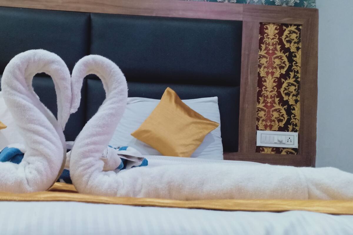 A bed with a heart-shaped towel arrangement, a wooden headboard, and decorative pillows.