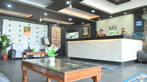 A reception area with a check-in counter, a wooden coffee table, and a seating area with chairs and a potted plant.