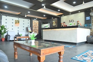 A reception area with a check-in counter, a wooden coffee table, and a seating area with chairs and a potted plant.