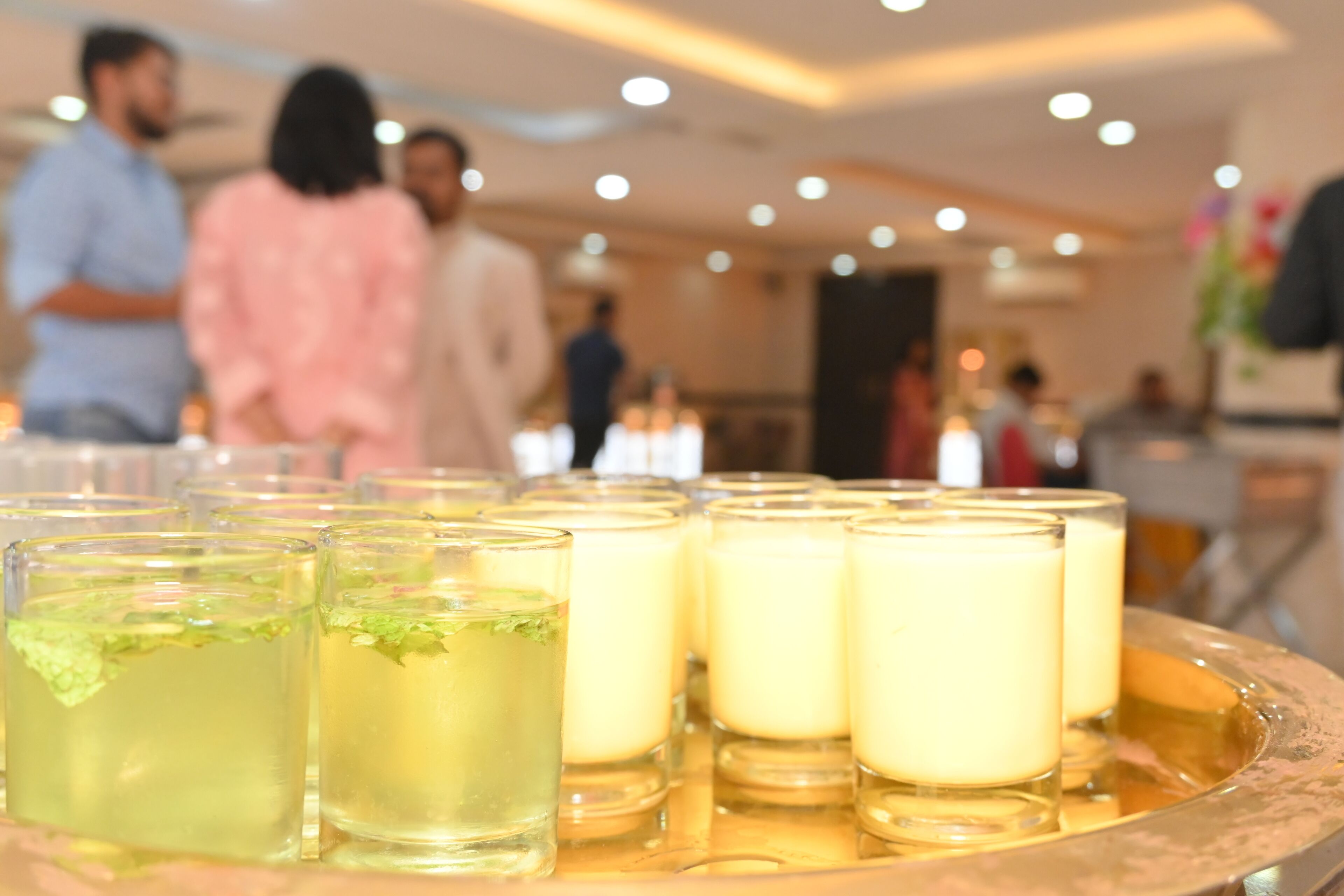Una bandeja con varios vasos de bebidas, incluyendo un brebaje verde con menta y una bebida blanca cremosa, en un ambiente interior bien iluminado.