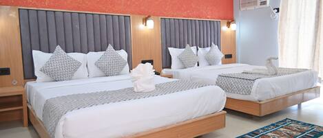 A hotel room with two beds, each with a grey headboard, white bedding, and patterned pillows. There is a decorative wall piece above the beds and a blue patterned rug on the floor.