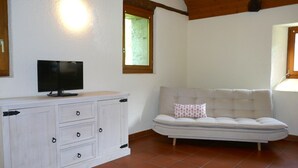 Een kamer met een wit kastje, een televisie, een comfortabele bank en een raam met uitzicht op groen.
