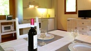 Een eettafel, gedekt met wijnglazen en een fles wijn, een televisie en een keuken op de achtergrond.