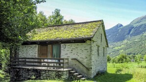 Een klein stenen huis met een mosgroen dak, een houten veranda en een stenen muur.