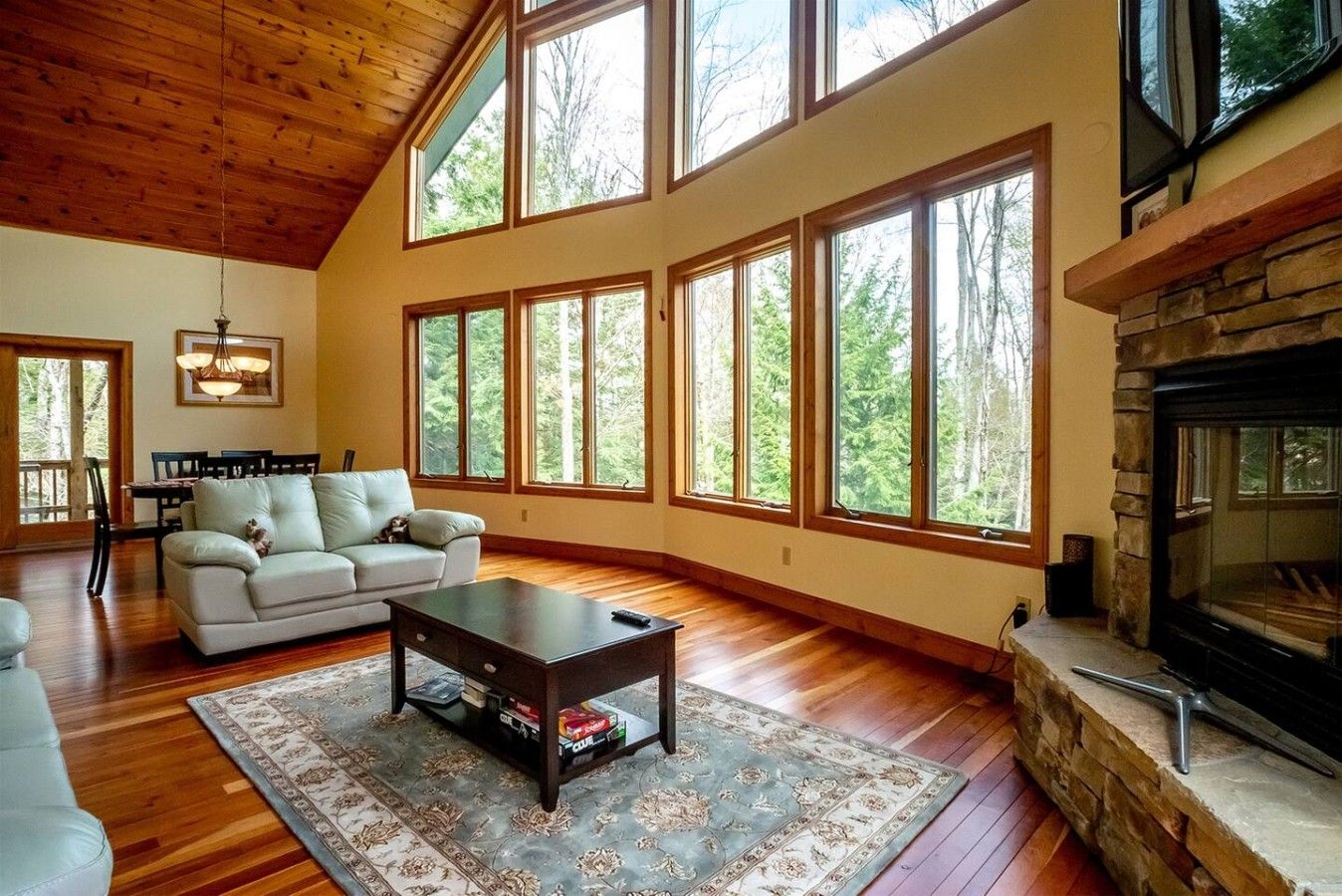 A spacious living room with a fireplace, large windows, and a high ceiling.