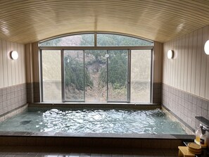 A spa room with a large window, a hot tub, and a view of a forested area.