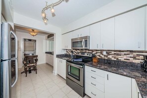 A modern kitchen with stainless steel appliances, white cabinetry, and a tiled backsplash.