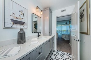 A modern bathroom with a large mirror, a bathtub, and a sink. There is a hallway leading to a bedroom with a balcony.