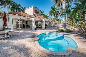 A pool area with a circular pool, lounge chairs, and palm trees.