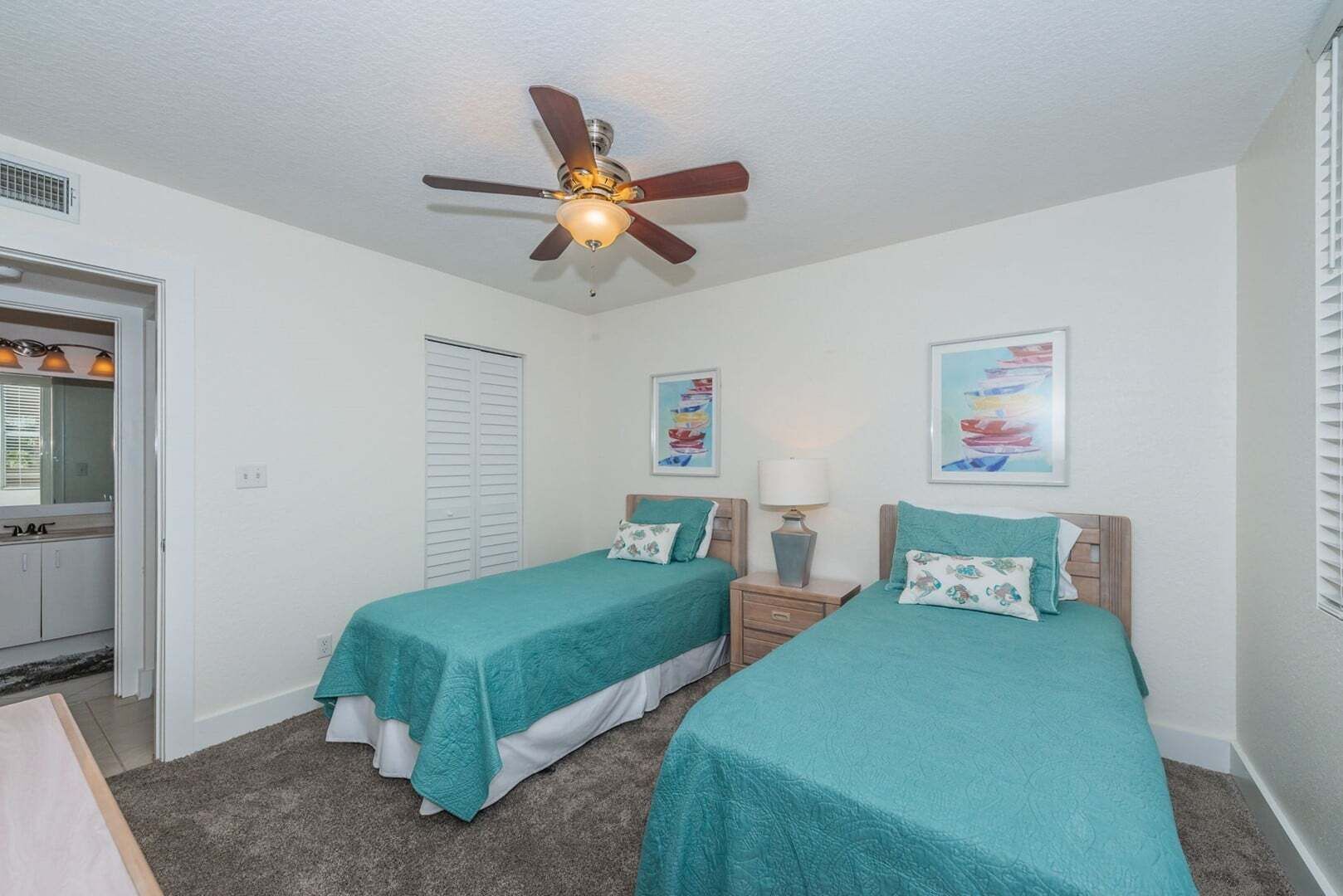 A bedroom with two single beds, a ceiling fan, a door with a window, and a wall with two framed pictures.