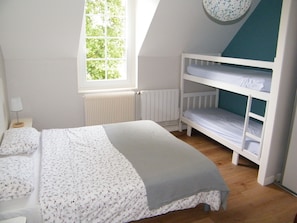 A bedroom with a bunk bed, a window with a view of trees, a radiator, and a bedside table with a lamp.