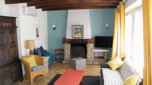 Ein gemütliches Wohnzimmer mit Kamin aus Stein, einer Couch, einem roten Tisch und einem Fernseher.