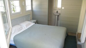 Ein Schlafzimmer mit Bett, Nachttisch, Fenster und einem Badezimmer mit Waschbecken.