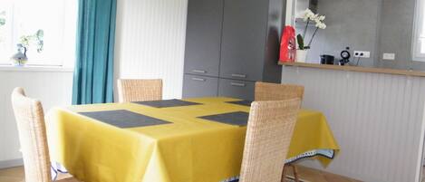 Un comedor con una mesa amarilla, cuatro sillas de mimbre, un armario gris y un tapete estampado.