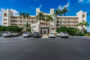 A hotel with a central entrance, multiple floors, and a parking lot with several cars.