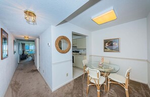A hallway leading to a dining area with wicker chairs, a glass table, and a woven mirror on the wall.