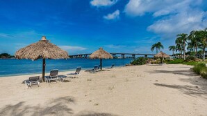 A beach with thatched umbrellas, lounge chairs, and a bridge in the background. - Waterfront 2BR condo in St. Petersburg with balcony, pool, and water views. (St Petersburg)