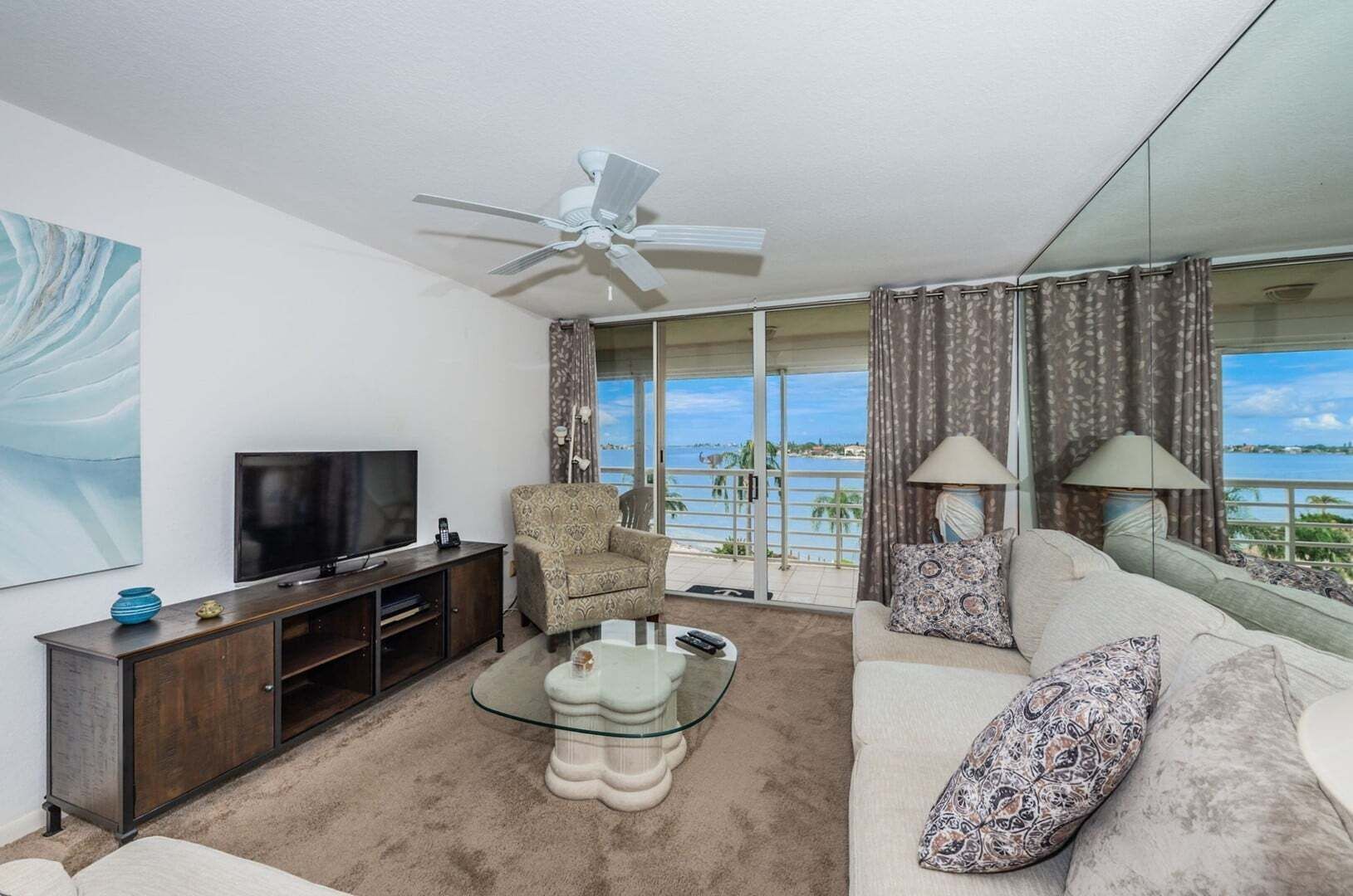 Una sala de estar con televisor, sofá, sillón y una mesa de centro de vidrio.