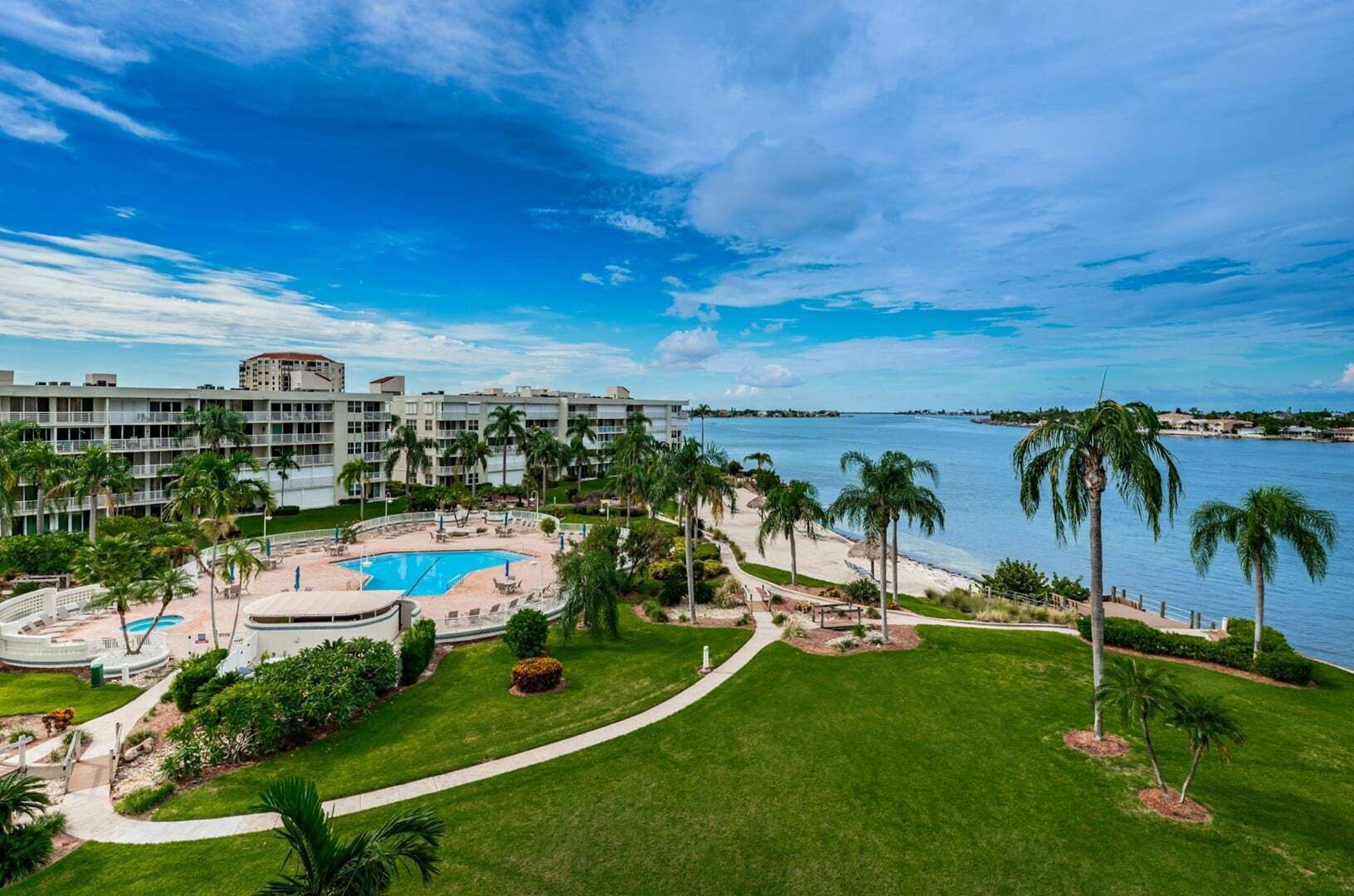 A resort with a pool, palm trees, and a view of the water.