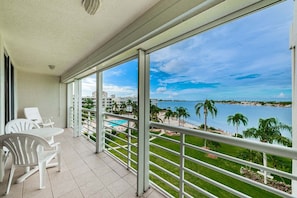 Un balcone con vista su una piscina e una spiaggia, sedie bianche e cielo sereno.