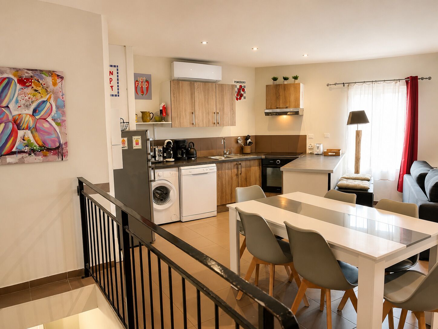 A modern kitchen with a washing machine, a coffee machine, and a dining area with a table and chairs.