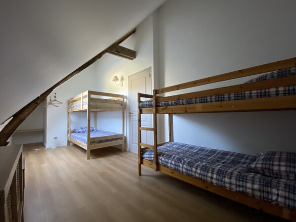 Une chambre de dortoir avec deux lits superposés, un plancher en bois, une porte blanche et un luminaire fixé au mur.