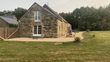 A stone building with a large window, a door, and a small patio area with a table and chairs.