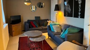 Un salon avec un canapé, une table basse, un téléviseur et des œuvres d’art accrochées au mur.