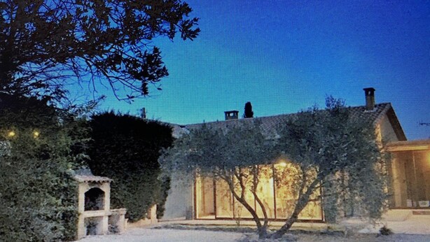Une maison avec une grande fenêtre, une cheminée et un arbre au premier plan.