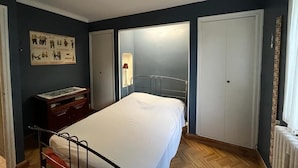 Une chambre à coucher avec un lit, une commode, une armoire et une affiche accrochée au mur.
